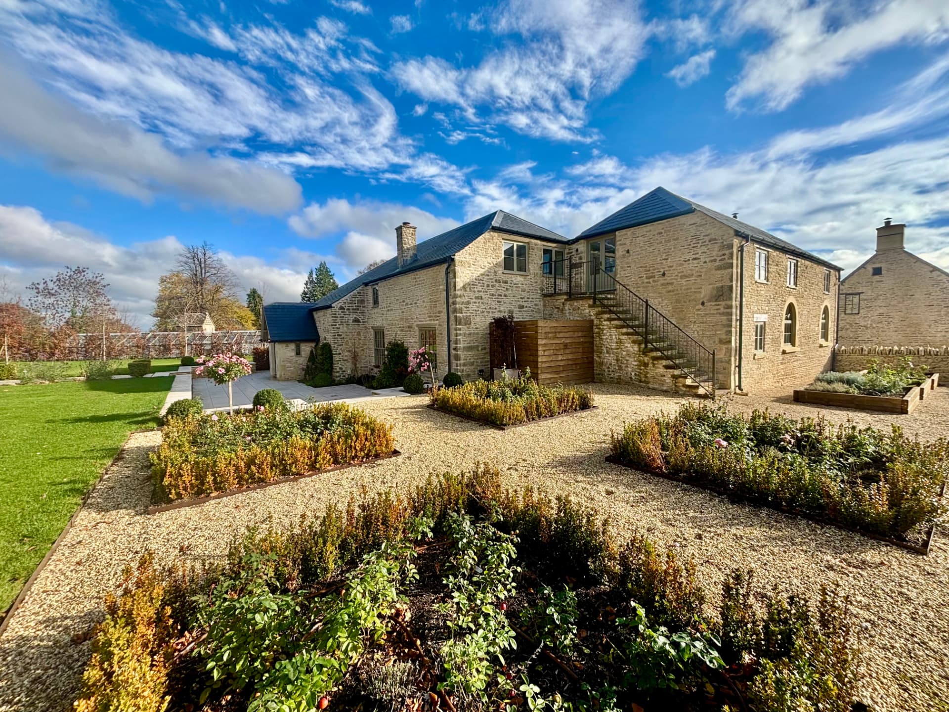 Converted Cotswold stone coach house with landscaped gardens and external lighting at dusk